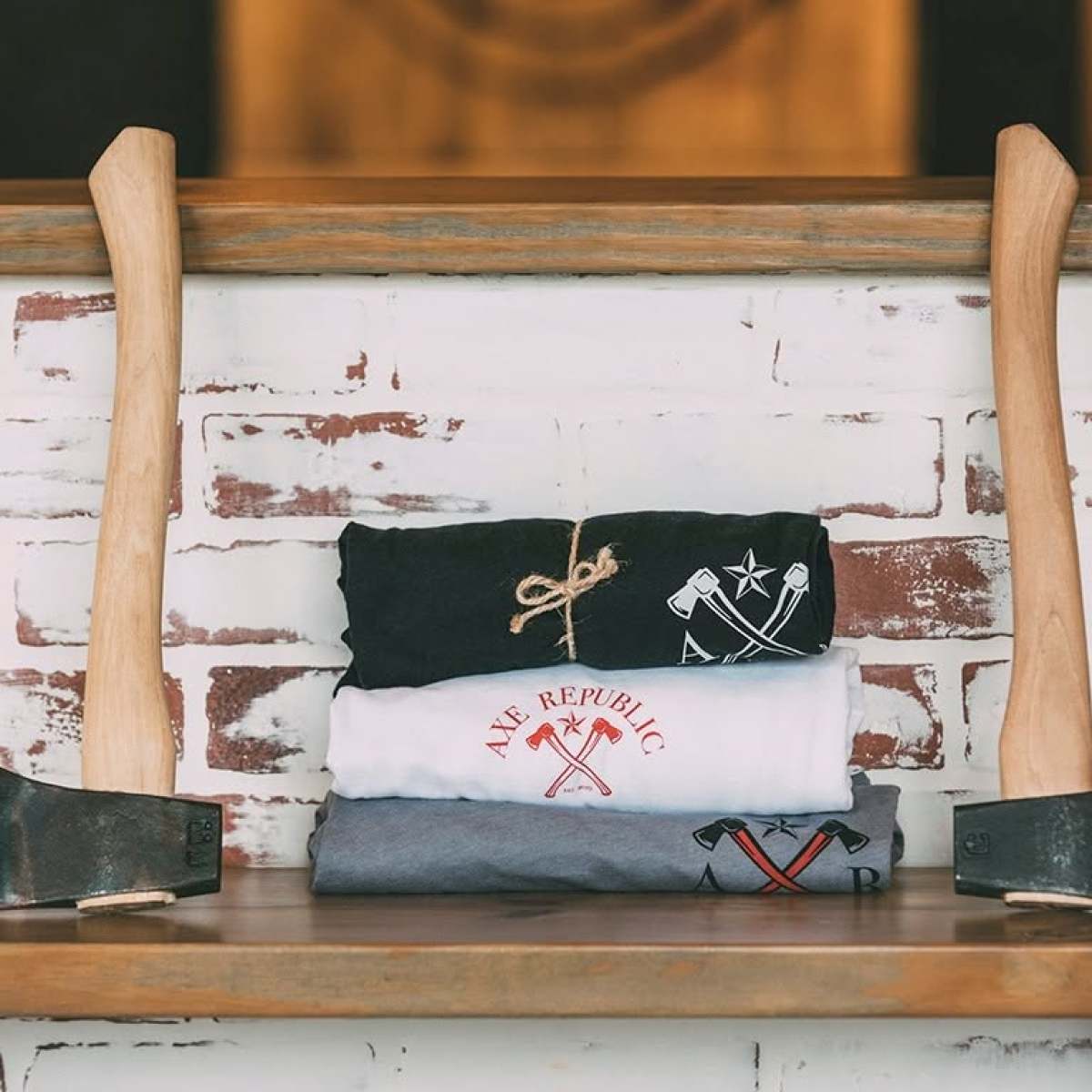 Two axes framing stacked t-shirts on a wooden shelf.