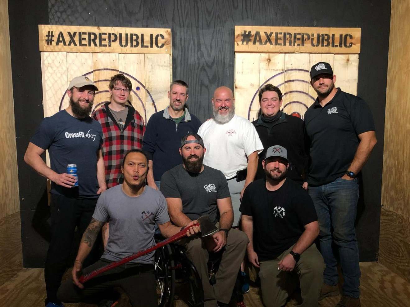 Group of nine people posing in front of axe-throwing targets indoors.
