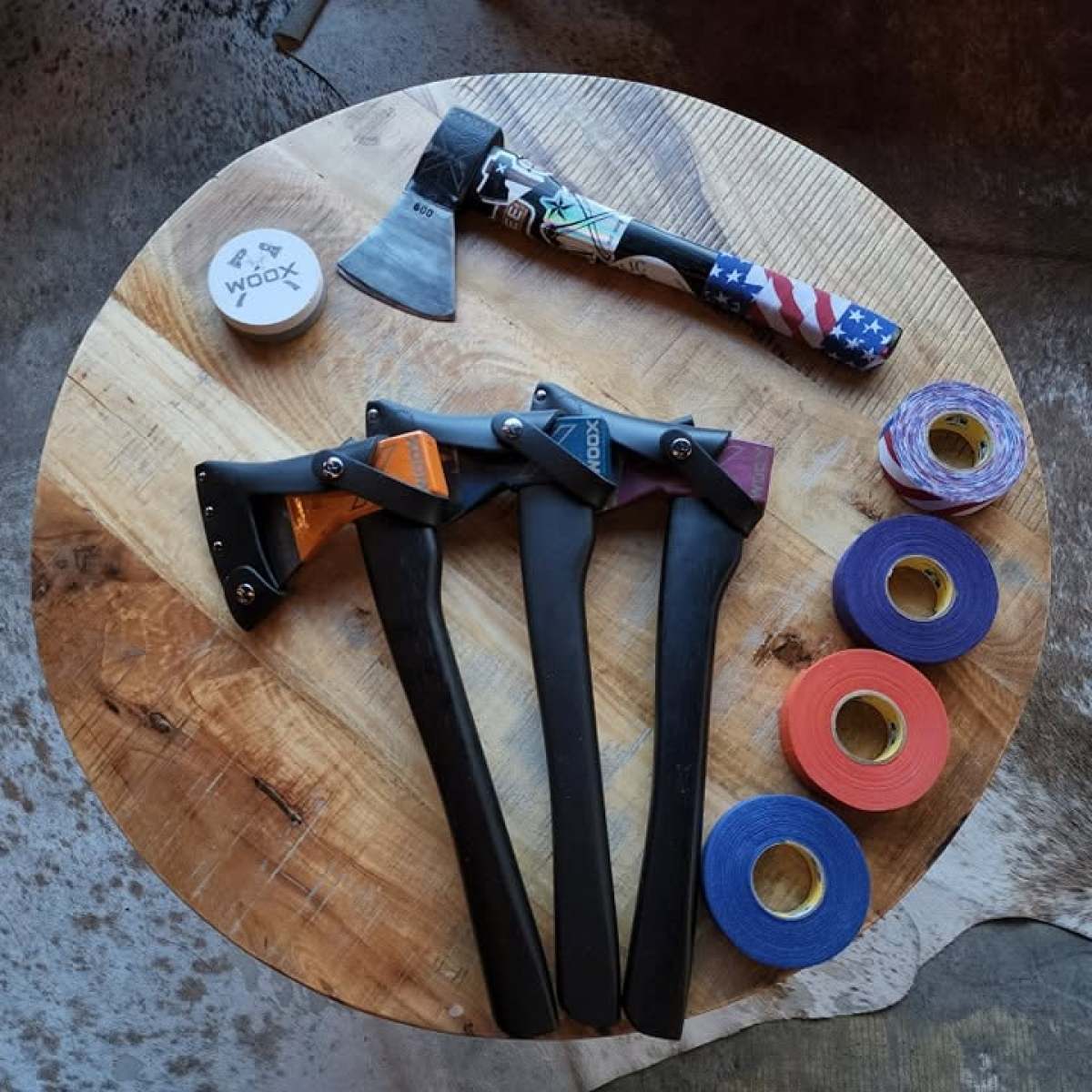 Four axes, rolls of tape, and a puck on a round wooden table.