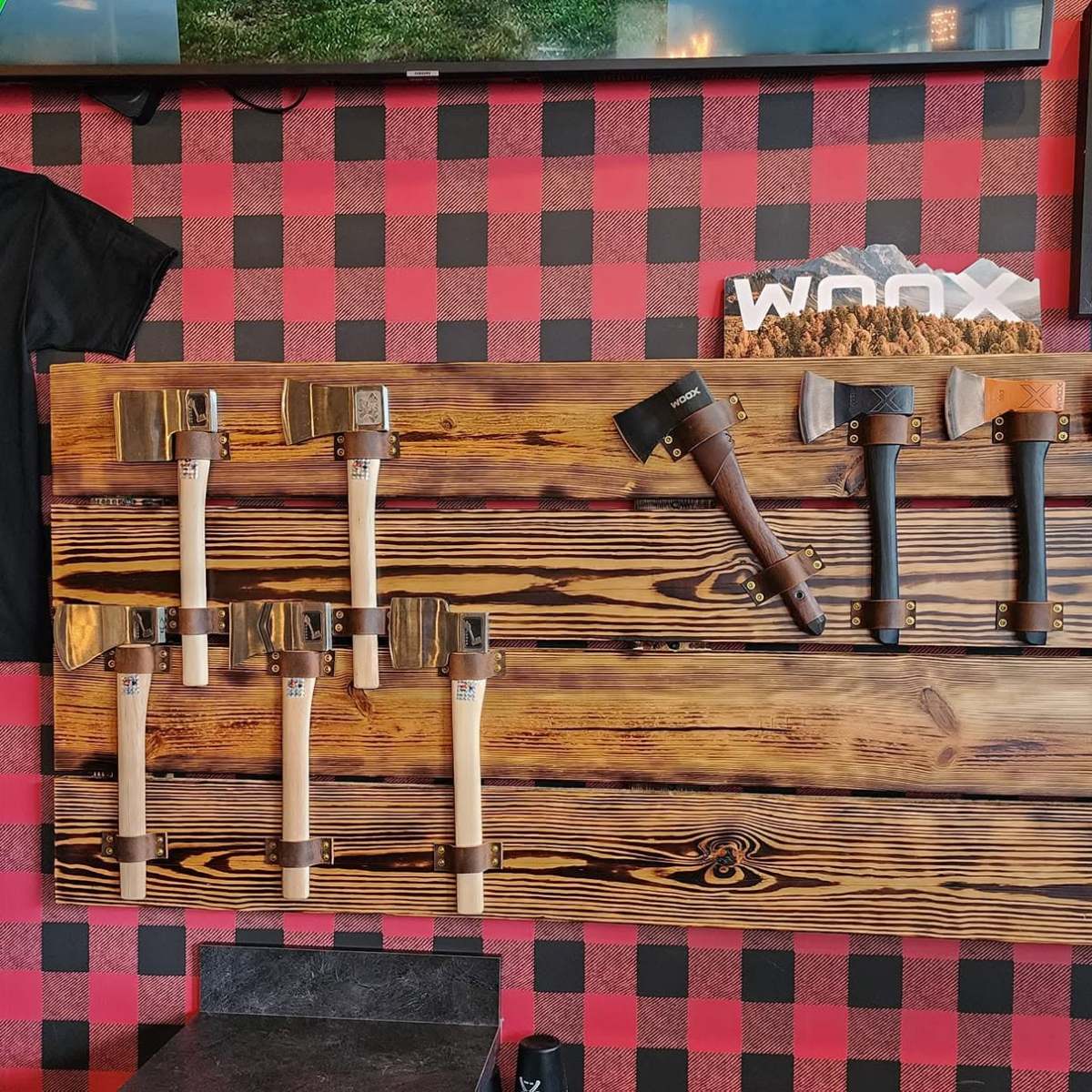 Wall display of axes and a shirt with 'Beer & Axes' slogan at an axe throwing venue.