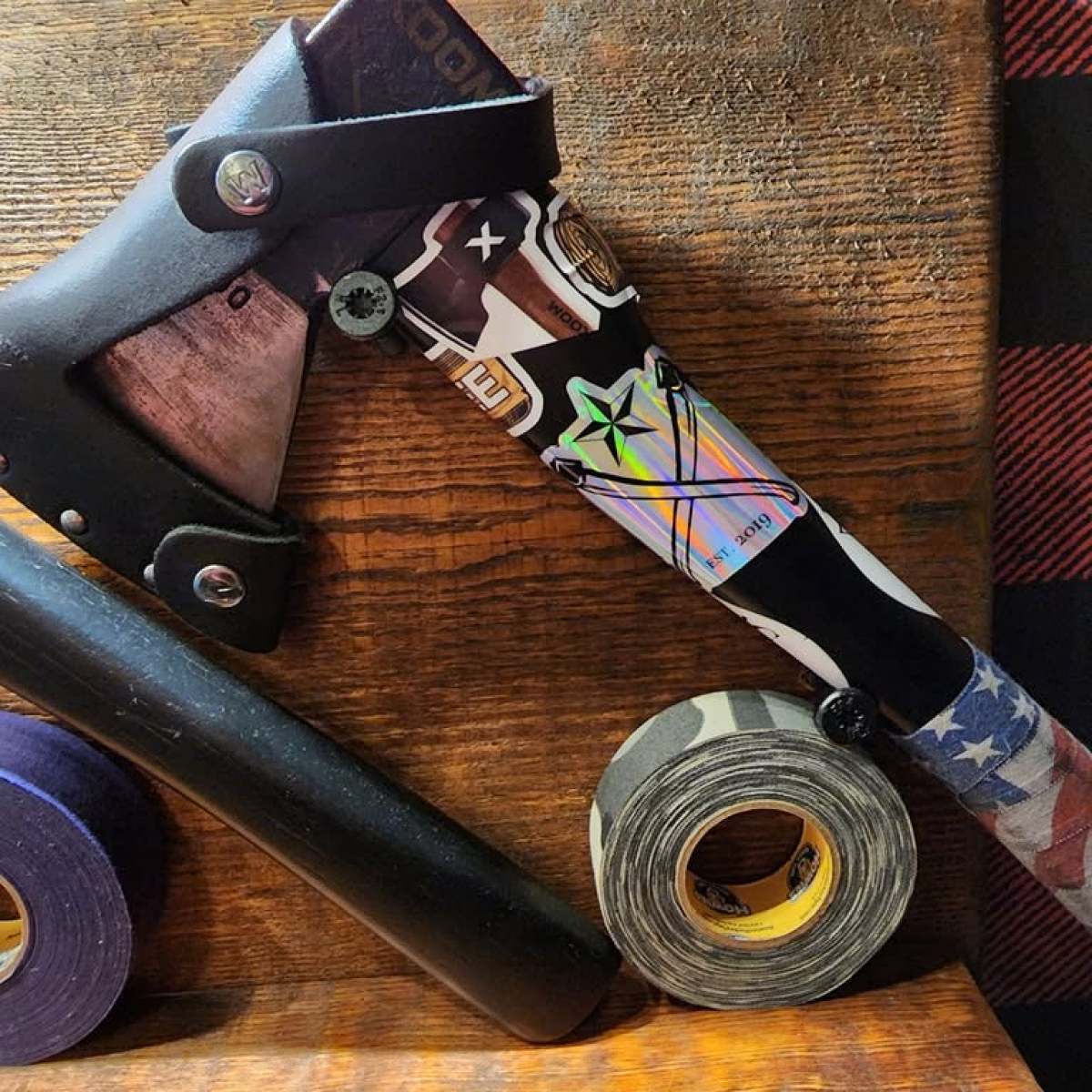 Decorative axe with custom handle on wooden surface, surrounded by tape rolls and a black tube.