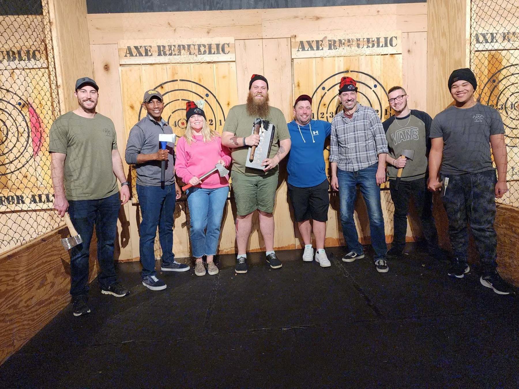 Group of people holding axes in an axe throwing venue, smiling and posing for a photo.
