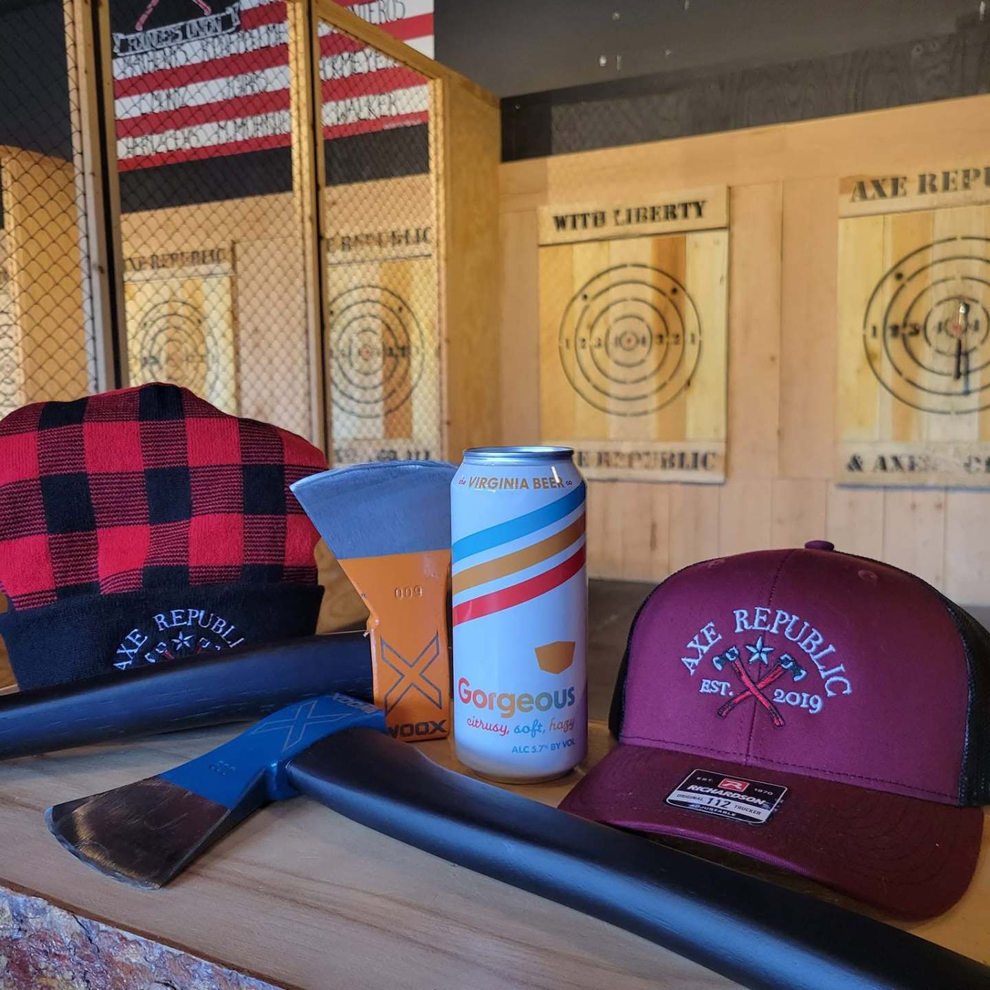 Axes, caps, and drinks on a table at an axe-throwing venue.