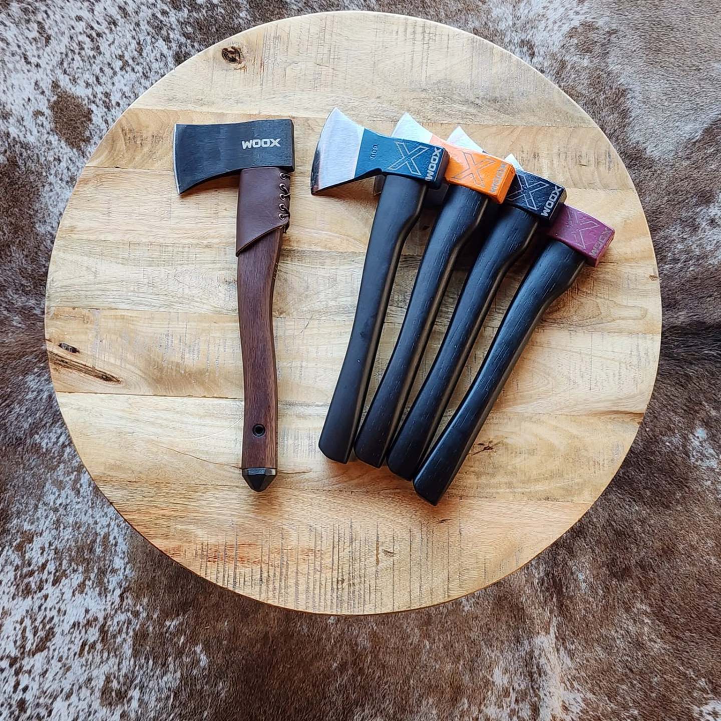 Five axes with colorful handles on a round wooden surface.