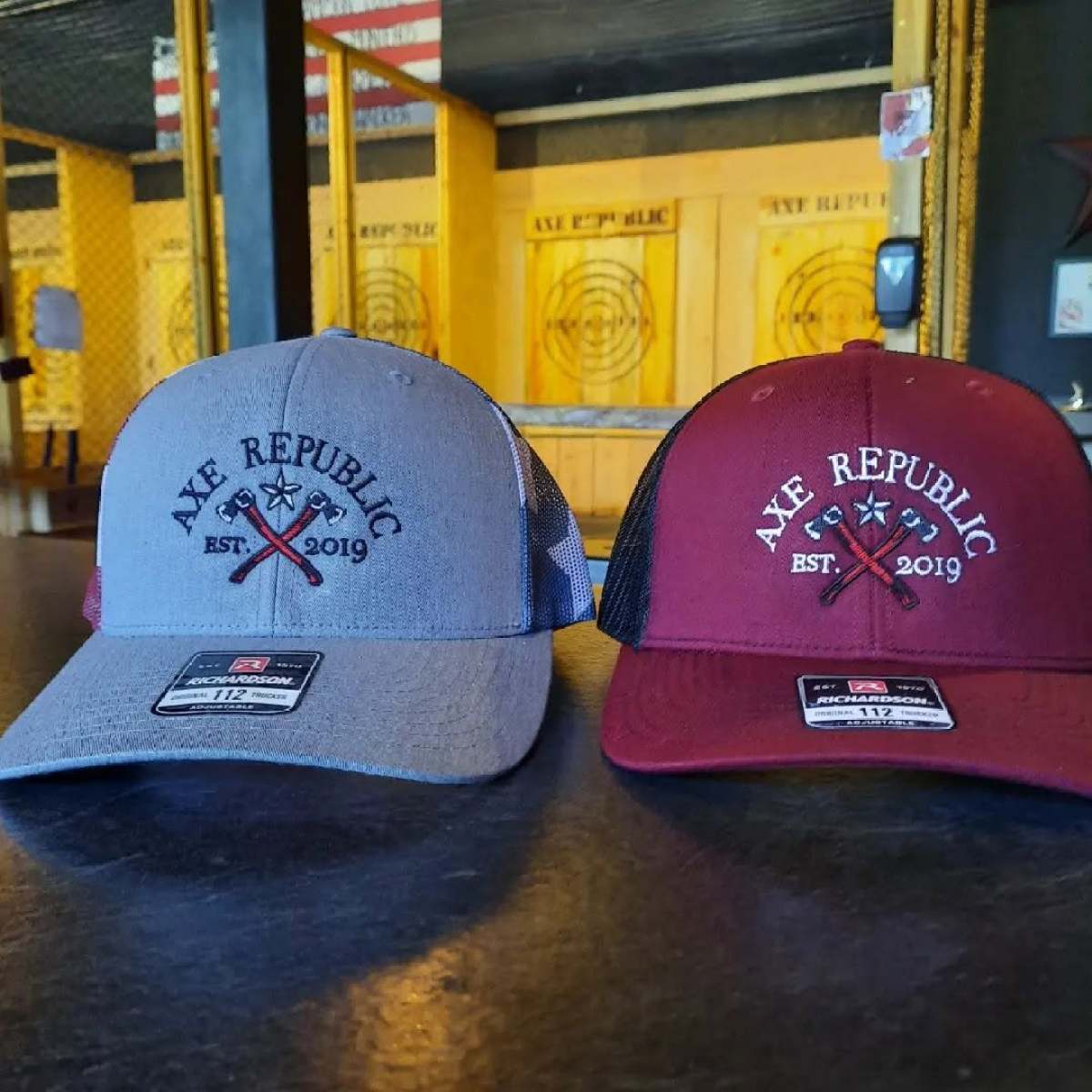 Two baseball caps with 'Axe Republic Est. 2019' logo on a countertop.