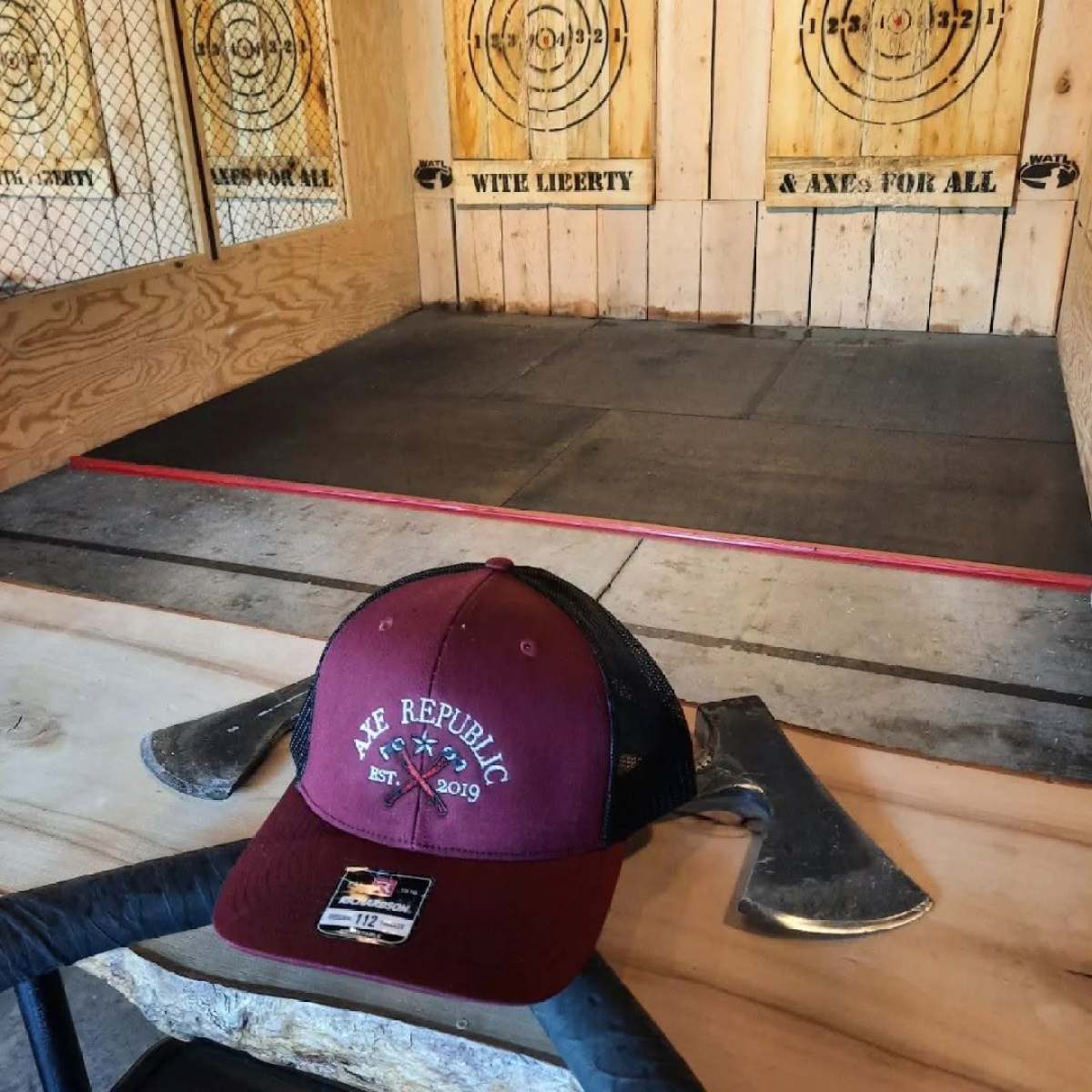 Axe throwing lanes with hat and axes on table in foreground.
