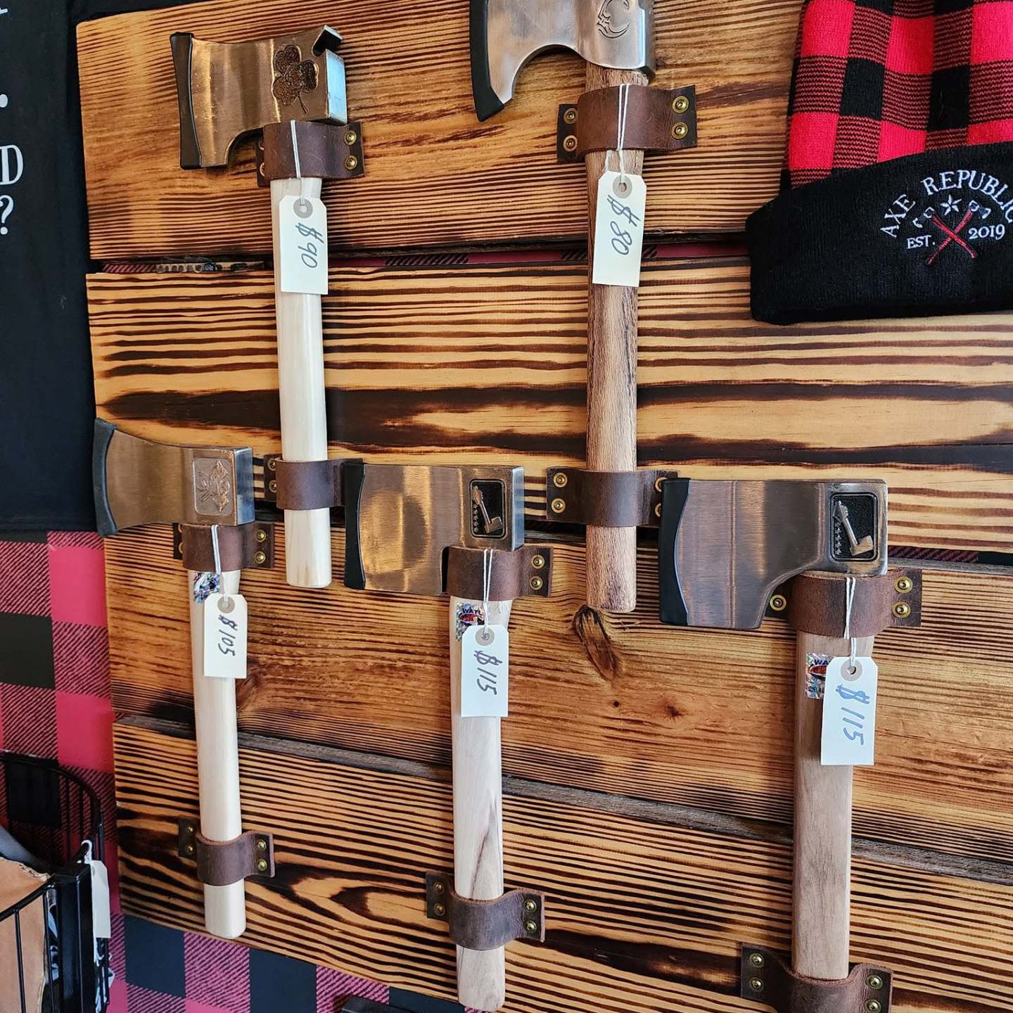 Wall display of axes and a red checkered beanie on wood background.