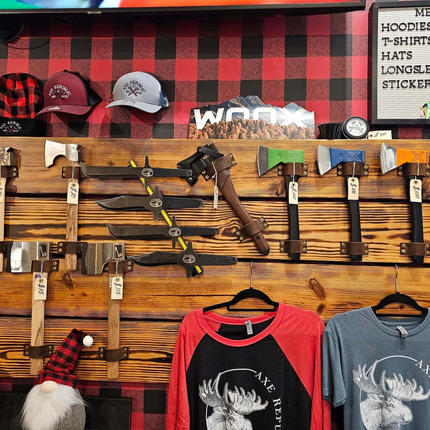 Wall display of axes, hats, shirts, and merch prices on wooden backdrop.