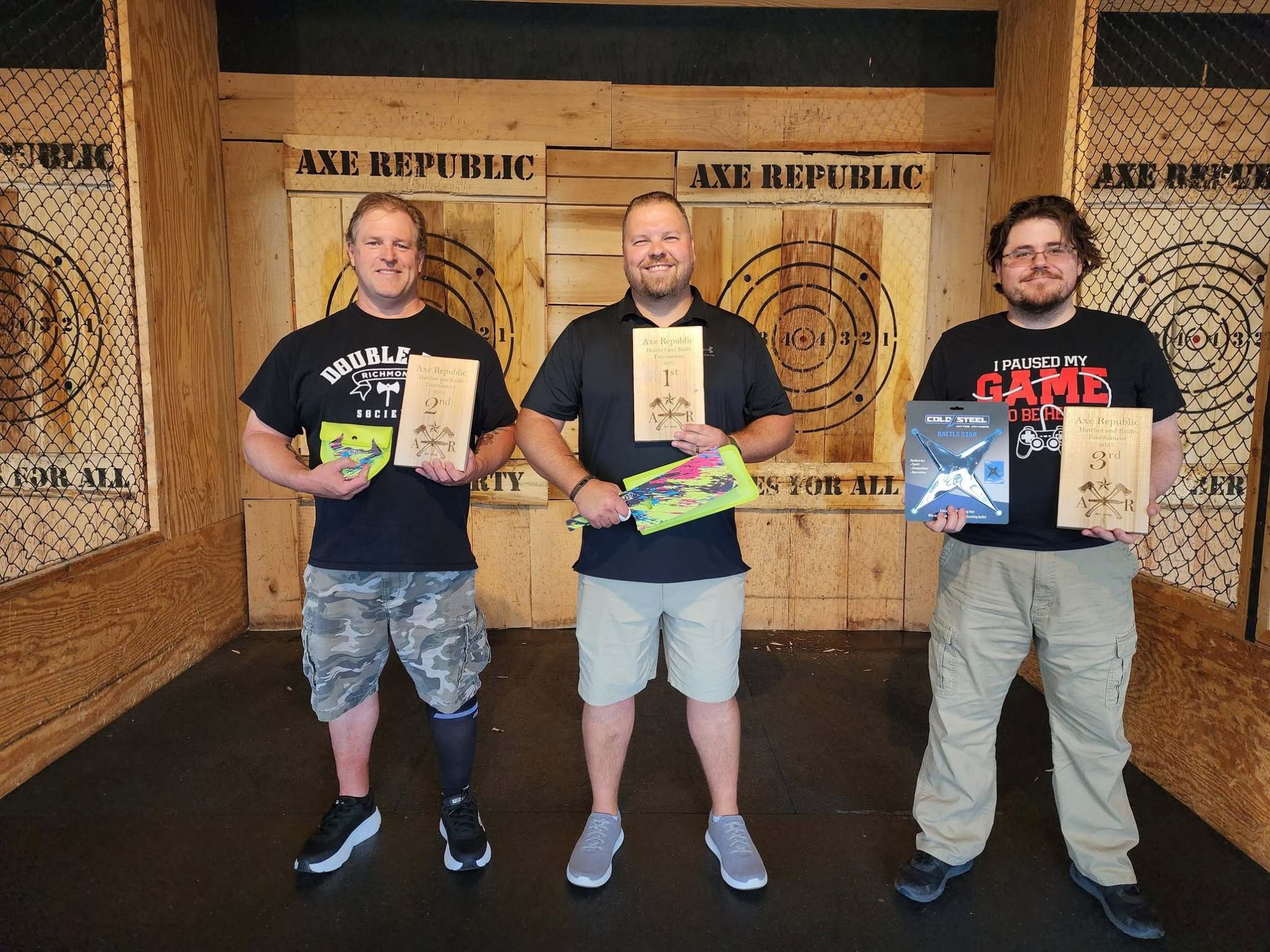Three men at Axe Republic holding awards, standing in front of target boards.
