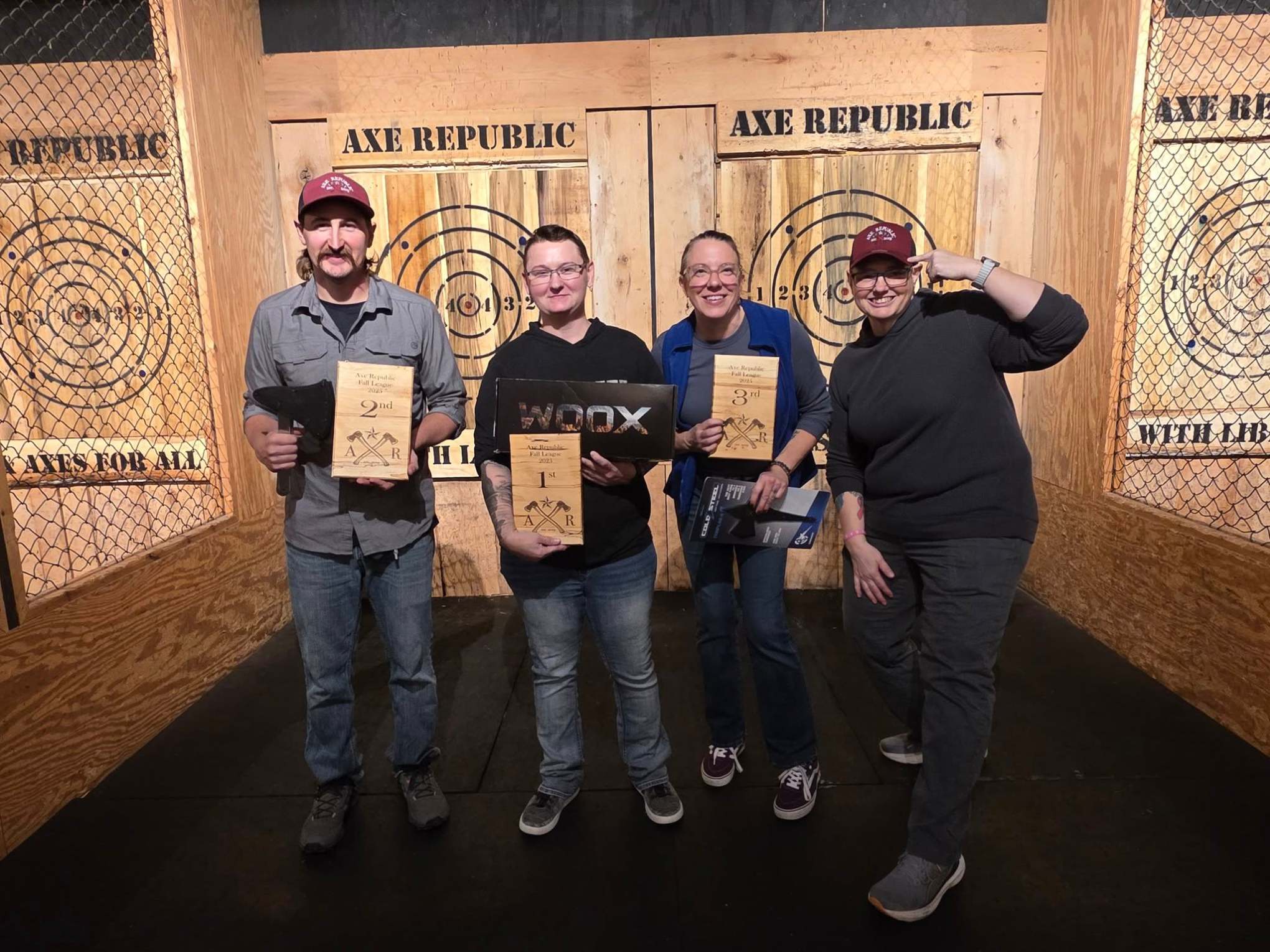 Four people smiling, holding awards at an axe throwing venue.