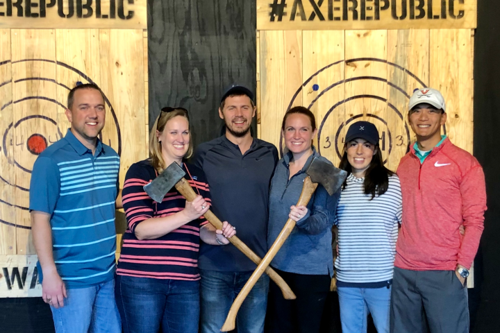 Group of six people holding axes in an axe-throwing venue.