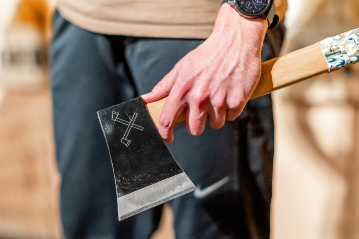 Person holding an axe with a wooden handle and crossed axes symbol on the blade.