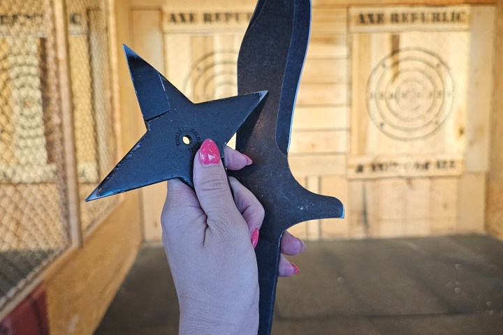 Hand holding knife and ninja star in axe-throwing range.