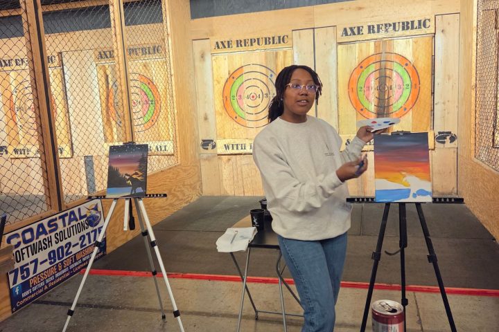 Person posing with a painting inside an axe-throwing venue.