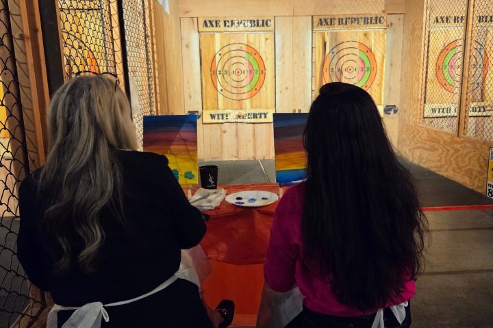 Two people sitting and painting targets at an indoor range.