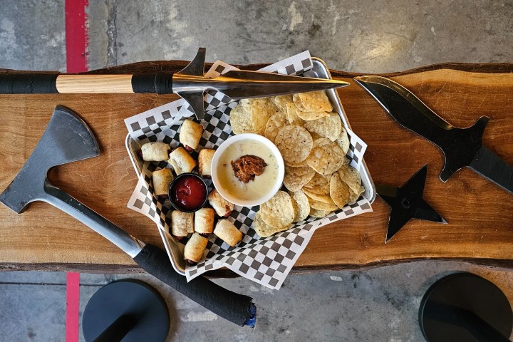 A tray with snacks surrounded by axes and throwing stars on a wooden table.