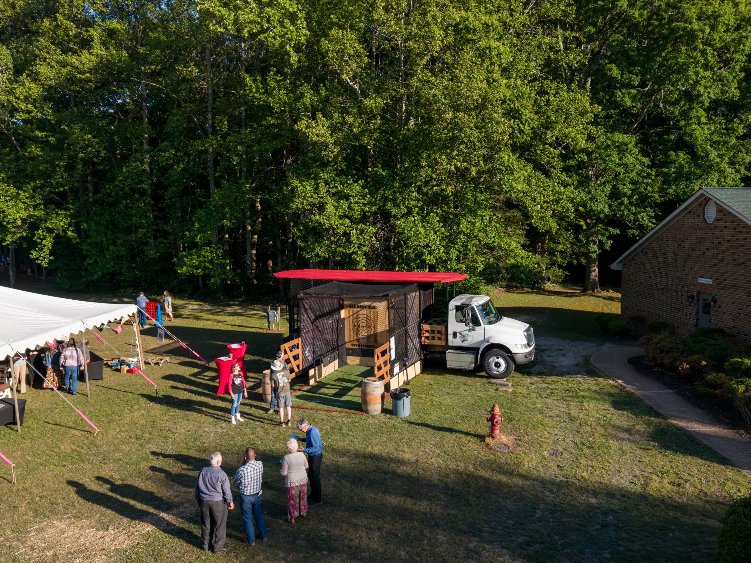 Outdoor event with a food truck, people, tent, and trees in background.
