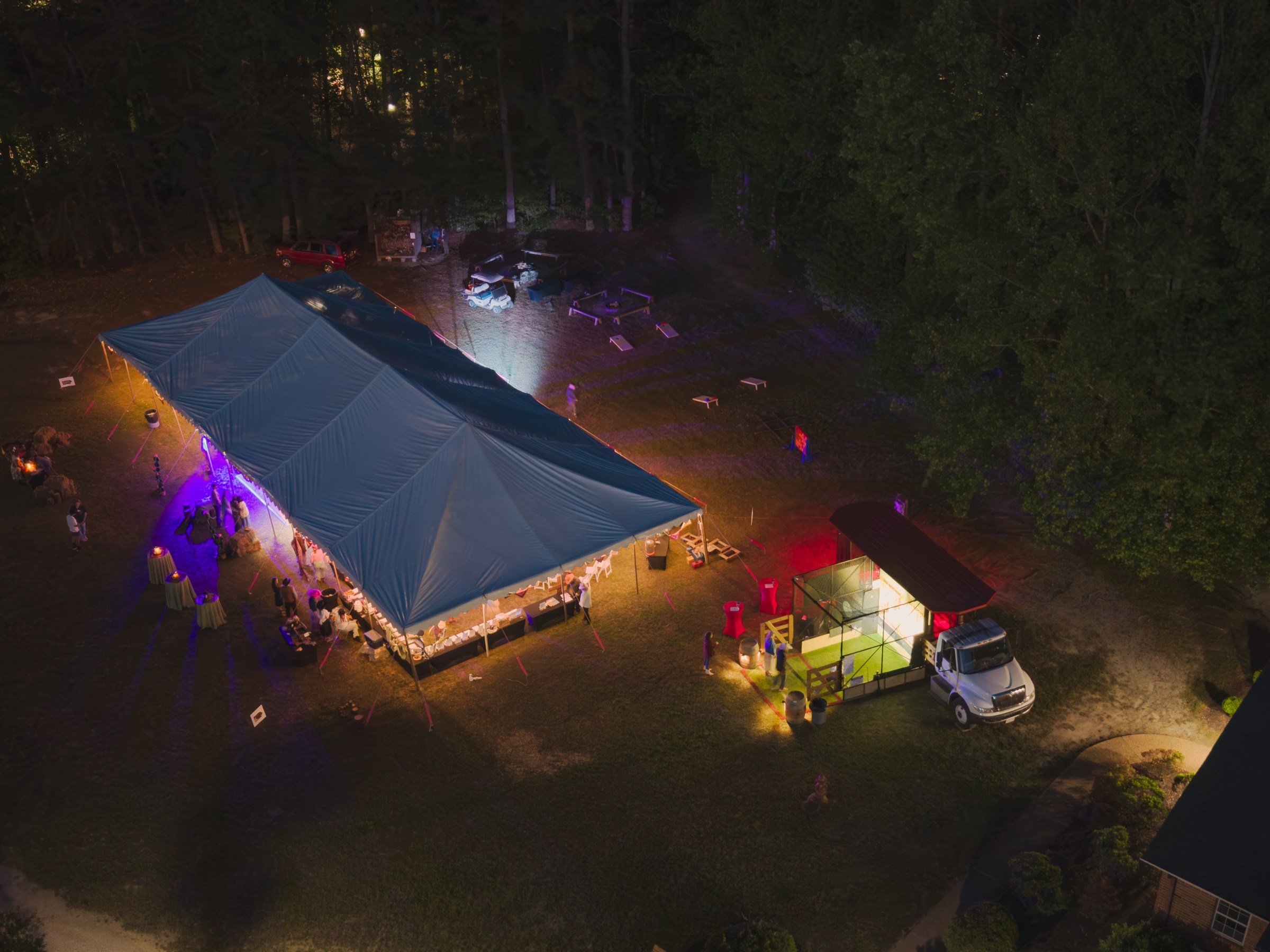 Night event with illuminated tents and food truck in wooded area.