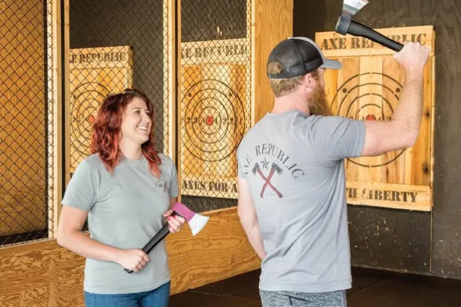 Two people in Axe Republic shirts holding axes in axe-throwing venue.