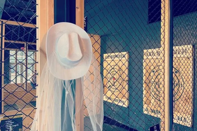 White hat with veil on wire fence near wooden target boards in axe-throwing venue.