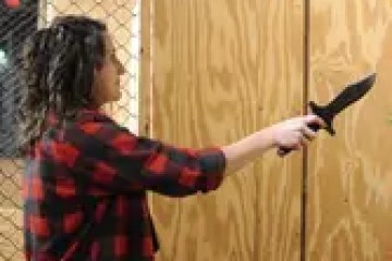 Person in red plaid shirt holding a knife in an axe-throwing venue.